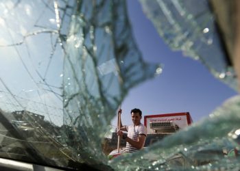 A Palestinian man is seen through a shuttered window of a car near an Israeli airstrikes