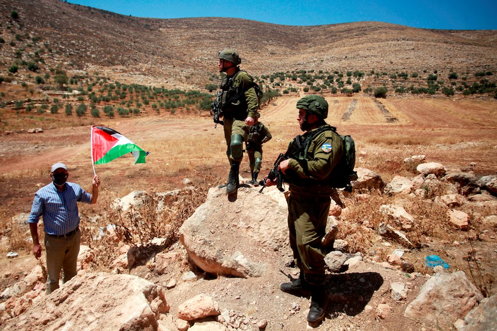 Palestinian man confronts Israeli forces and raises Palestine flag during a protest against the establishment of Israeli outposts, in Beit Dajan, east of the West Bank city of Nablus, on July 28, 2023.
