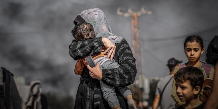 Seorang ibu Palestina melindungi anaknya dari asap tebal dengan menutupi wajah sang anak, saat mereka mengungsi dari wilayah utara Gaza menuju bagian tengah dan selatan Jalur Gaza."