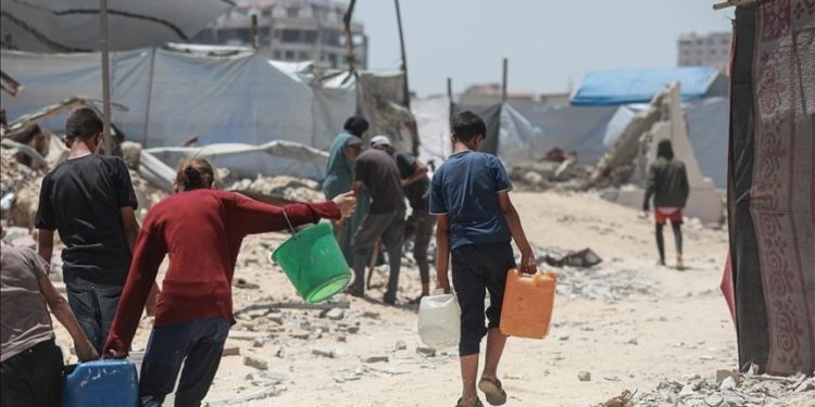 "Warga Palestina, termasuk anak-anak, berjalan di antara reruntuhan sambil membawa jeriken air di kamp pengungsian Gaza."