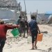 "Warga Palestina, termasuk anak-anak, berjalan di antara reruntuhan sambil membawa jeriken air di kamp pengungsian Gaza."