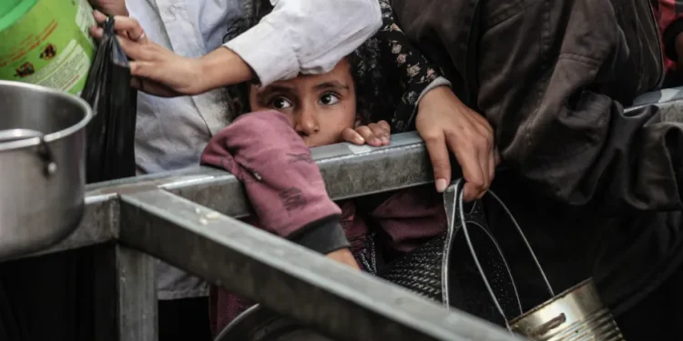 Warga Palestina, termasuk anak-anak, menunggu dengan panci untuk menerima makanan hangat yang didistribusikan oleh lembaga amal, sementara mereka berjuang melawan kelaparan akibat blokade makanan Israel di kamp pengungsi Nuseirat di Deir al-Balah, Gaza, pada 15 Oktober 2025. [Moiz Salhi/Anadolu via Getty Images]