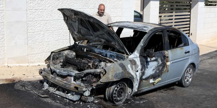 Seorang pria memeriksa kendaraan yang dibakar oleh pemukim Israel dalam serangan di desa Taybeh, Tepi Barat, pada Juli 2025 (Zain Jaafar/AFP)