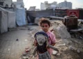 Seorang gadis Palestina yang terusir memegang boneka sambil bermain di luar tenda keluarganya di kamp pengungsian dekat pelabuhan di Kota Gaza, pada 19 Oktober 2025. [Foto oleh Majdi Fathi/NurPhoto via Getty Images]
