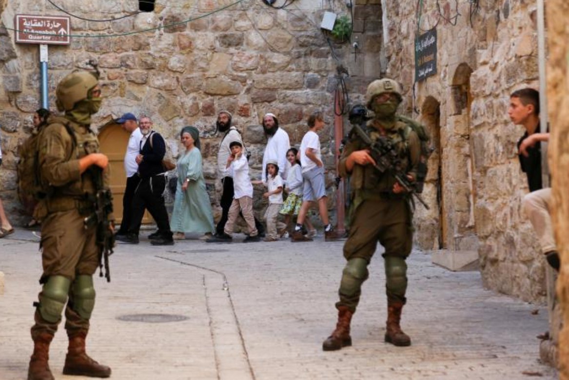 Tentara Israel yang mengawal para pemukim kolonial membatasi kebebasan bergerak warga Palestina di Kota Tua Al-Khalil/Hebron, Tepi Barat (18/10). Serangan berulang ini merupakan bagian dari strategi panjang Israel untuk mengendalikan kota tersebut, khususnya wilayah di sekitar Masjid Ibrahimi. (Mosab Shawer/ActiveStill)