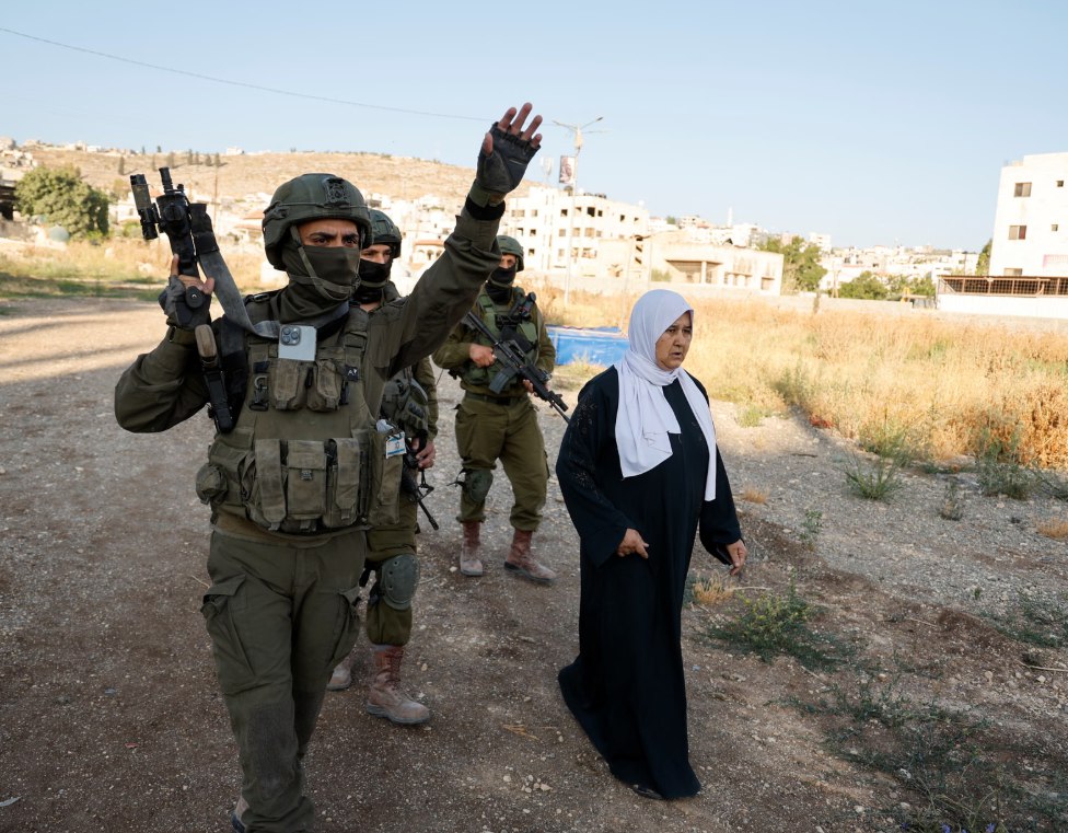 Tentara Israel menghentikan warga Palestina yang hendak berziarah ke pemakaman di Kamp Jenin (24/10). Penduduk Palestina di Jenin kini semakin sulit untuk menjalani hidup yang bebas karena pembatasan yang diberlakukan Israel. Tentara Israel telah menduduki Kamp Jenin sejak Januari, mengusir 14.000 penduduk dari rumah mereka dan membangun tanggul tanah serta penghalang untuk memisahkan Jenin dari bagian kota Palestina lainnya. (Raneen Sawafta/Reuters/The Guardian)