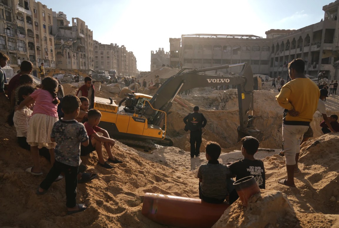 Warga Palestina menyaksikan alat berat dan beberapa pekerja dari Mesir yang bertugas mencari jenazah tahanan Israel di Kota Hamad, Khan Younis (26/10). Hamas telah memperluas pencarian jenazah sandera di Jalur Gaza, setelah Mesir mengerahkan tim ahli dan alat berat untuk membantu mengevakuasi mereka. (Jehad Alshrafi/AP)