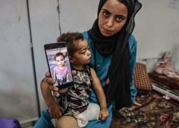 Seorang ibu di Gaza menunjukkan foto anaknya sebelum kakinya diamputasi karena serangan Israel (The New Arab)
