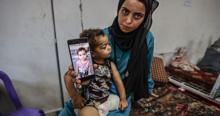 Seorang ibu di Gaza menunjukkan foto anaknya sebelum kakinya diamputasi karena serangan Israel (The New Arab)