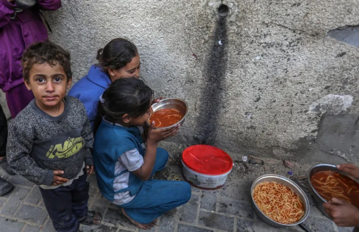 Warga Palestina yang terlantar menerima makanan hangat yang didistribusikan oleh sebuah lembaga amal di wilayah al-Mawasi, Khan Younis, Gaza (30/11). Israel hanya mengizinkan tidak lebih dari 200 truk bantuan masuk ke Gaza per hari dari 600 truk yang disepakati dalam kesepakatan gencatan senjata. Kantor Media Pemerintah Gaza memperingatkan bahwa tingkat malnutrisi di antara penduduk Gaza telah melampaui 90 persen. [Abed Rahim Khatib/ Anadolu/ Al Jazeera/ TRT)