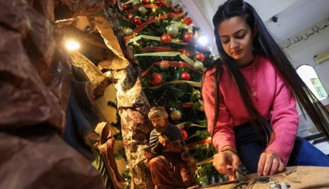 Seorang anak perempuan menghias pohon Natal di Gereja Keluarga Kudus di Gaza (MEE)