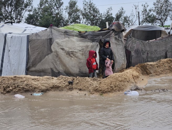 Dua anak berdiri menyaksikan banjir di depan tenda pengungsian (The Guardian)