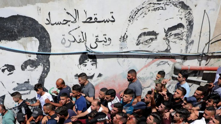 Warga Palestina melewati graffiti bergambar Ghassan Kanafani (kiri) dan salah satu perkataannya yang bersejarah, “Jasad dapat pergi, tetapi gagasan tetap bertahan” (The Markaz)
