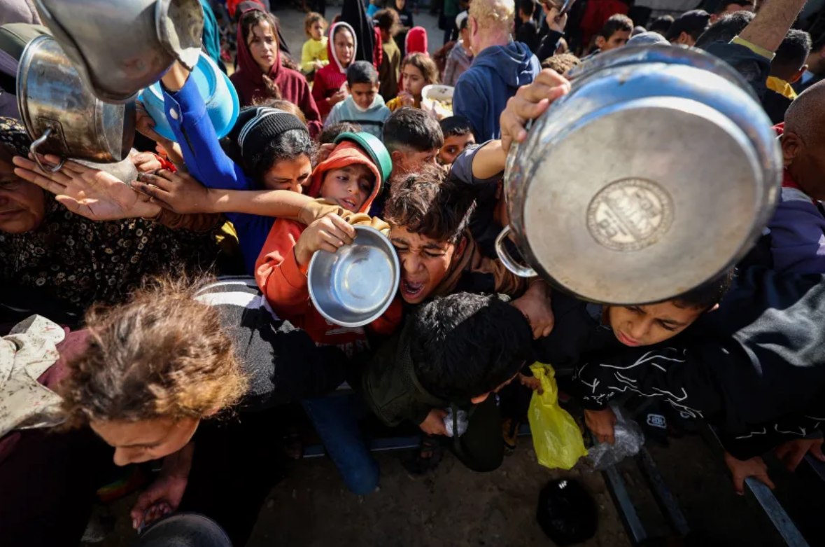 Para pengungsi Palestina berkumpul untuk menerima porsi makanan di dapur amal di kamp pengungsi Nuseirat di Jalur Gaza tengah pada 20 Desember 2025. (Eyad Baba/AFP/CNN)