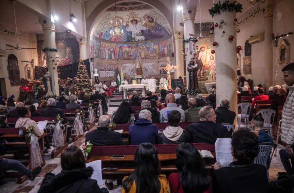 Umat Kristen di Gaza menghadiri misa Malam Natal di Gereja Keluarga Kudus di pusat Kota Gaza (24/12). Mereka menyalakan pohon natal untuk pertama kalinya setelah dua tahun agresi genosida. Jemaat memenuhi aula utama. Mereka berbahagia – bukan hanya karena Natal tetapi juga karena mereka masih hidup. (Abdelhakim Abu Riash/ Al Jazeera)