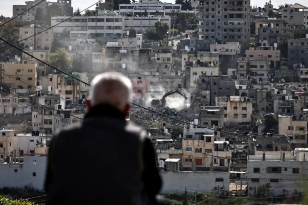 Warga Kamp Pengungsi Palestina Nur Shams menyaksikan rumah mereka dihancurkan oleh ekskavator militer Israel (31/12). Peningkatan operasi militer Israel dan kekerasan pemukim di Tepi Barat telah menghancurkan lebih banyak bangunan dan infrastruktur Palestina, membunuh 1.102 warga dan melukai 9.034 lainnya sejak Oktober 2023. (Zain Jaafar/AFP)