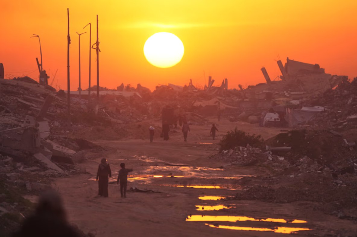 Warga Palestina berjalan melewati reruntuhan bangunan yang hancur, saat matahari terbenam di atas Kota Gaza (4/1). Mereka berharap mimpi buruk tentang kehancuran ini akan berakhir sehingga dapat menjalani kehidupan normal; listrik kembali menyala, jalanan kembali normal, dan dapat menyaksikan wilayah mereka bersih tanpa tenda-tenda yang berjejer di sepanjang jalan. (Jehad Alshrafi/ AP Photo/ The Arab Weekly)