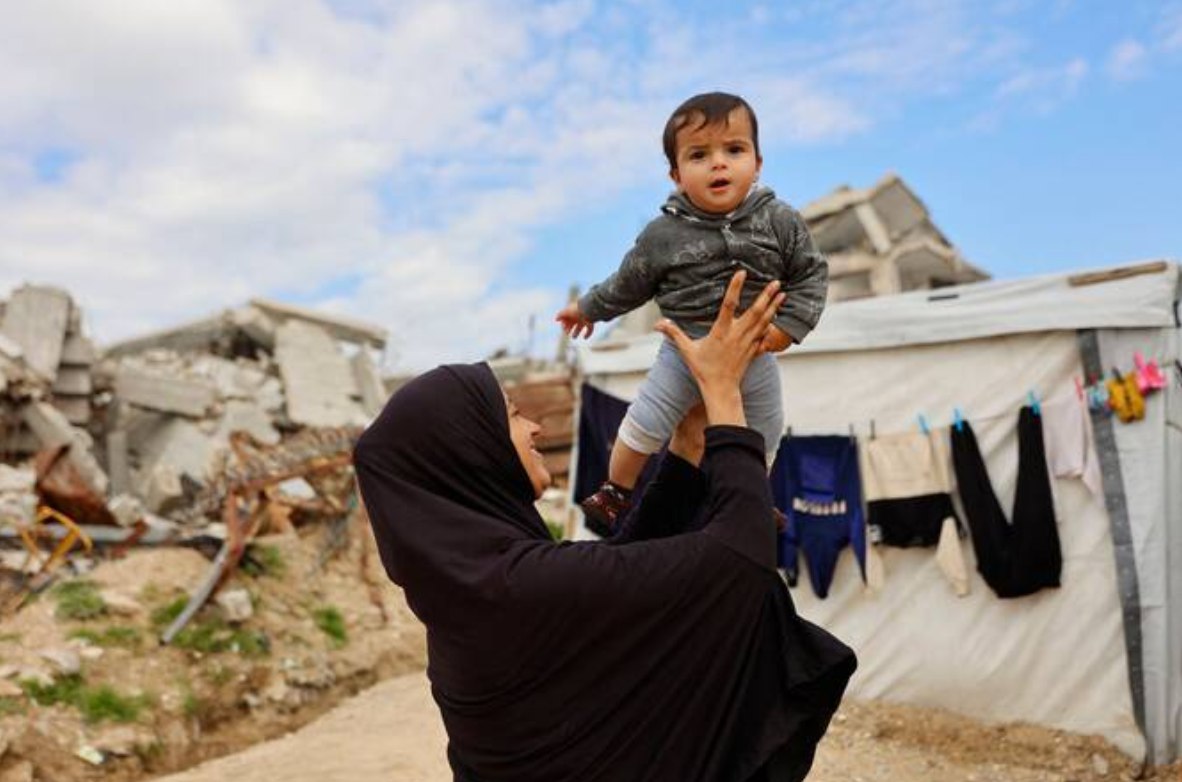 Seorang ibu Palestina bermain dengan anaknya di luar tenda pengungsian di Jabalia, utara Gaza (17/1). Warga terpaksa tinggal di sekitar reruntuhan bangunan yang dihancurkan militer Israel, di tengah blokade Israel terhadap keperluan bahan bangunan, caravan, dan tenda darurat layak guna. (AFP/ Arab News)
