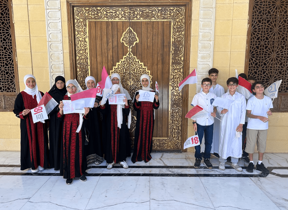 Para penghafal Palestina binaan Sahabat Adara berkumpul di depan markaz Al-Qur'an sambil membawa bendera Merah Putih, merayakan Hari Kemerdekaan ke-81 Republik Indonesia.